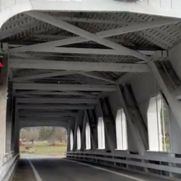 The bridge is a classic wooden covered bridge, built using a Howe truss design, a common engineering style for early 20th-century bridges. 